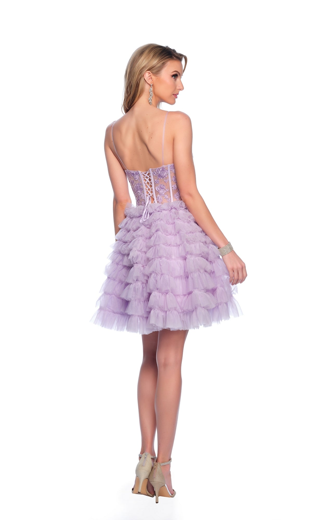 A woman stands with her back to the camera in the Dave and Johnny Ruffled Purple Hoco Dress 11766, featuring a short length, corset-style bodice, lace-up back, and ruffled skirt. She accessorizes with heels, earrings, and a bracelet.